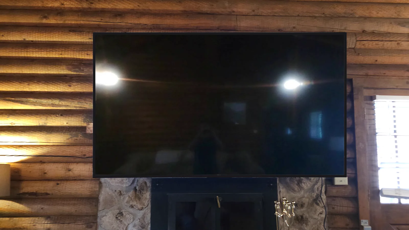 Large TV mounted on a log cabin wall above a stone fireplace